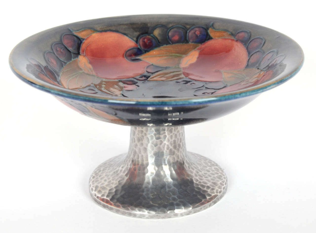 This piece was made by William Moorcroft for Liberty & Co. of London in about 1920. Combining a pottery dish in the pomegranate pattern with a planished pewter base it is 9.5 cm high by 17.5 cm in diameter. It was part of Liberty's Tudric Pewter