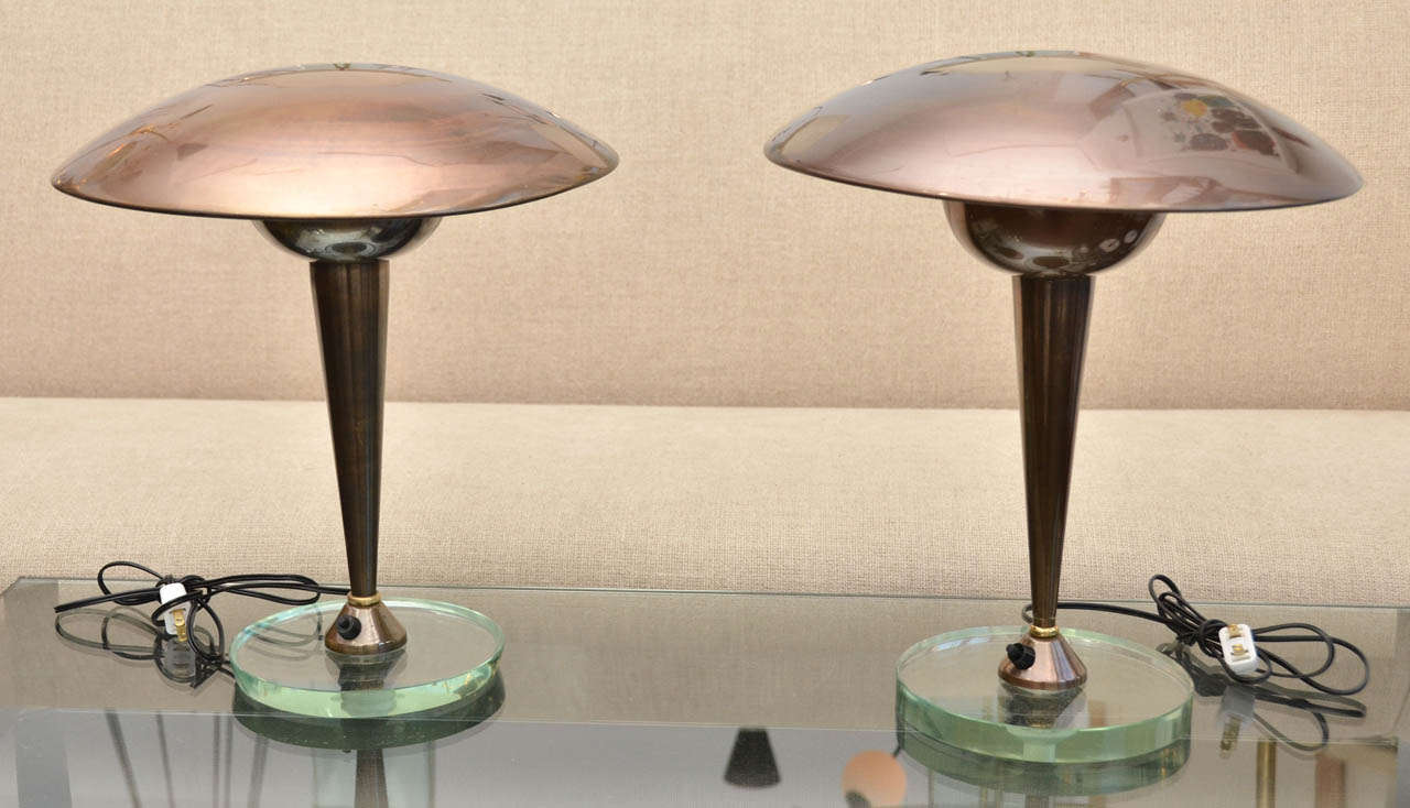 Pair of table lamps In the Style of  Stilnovo.  An adjustable brass circular shade connected to a cone shaped stem standing on a round glass base.