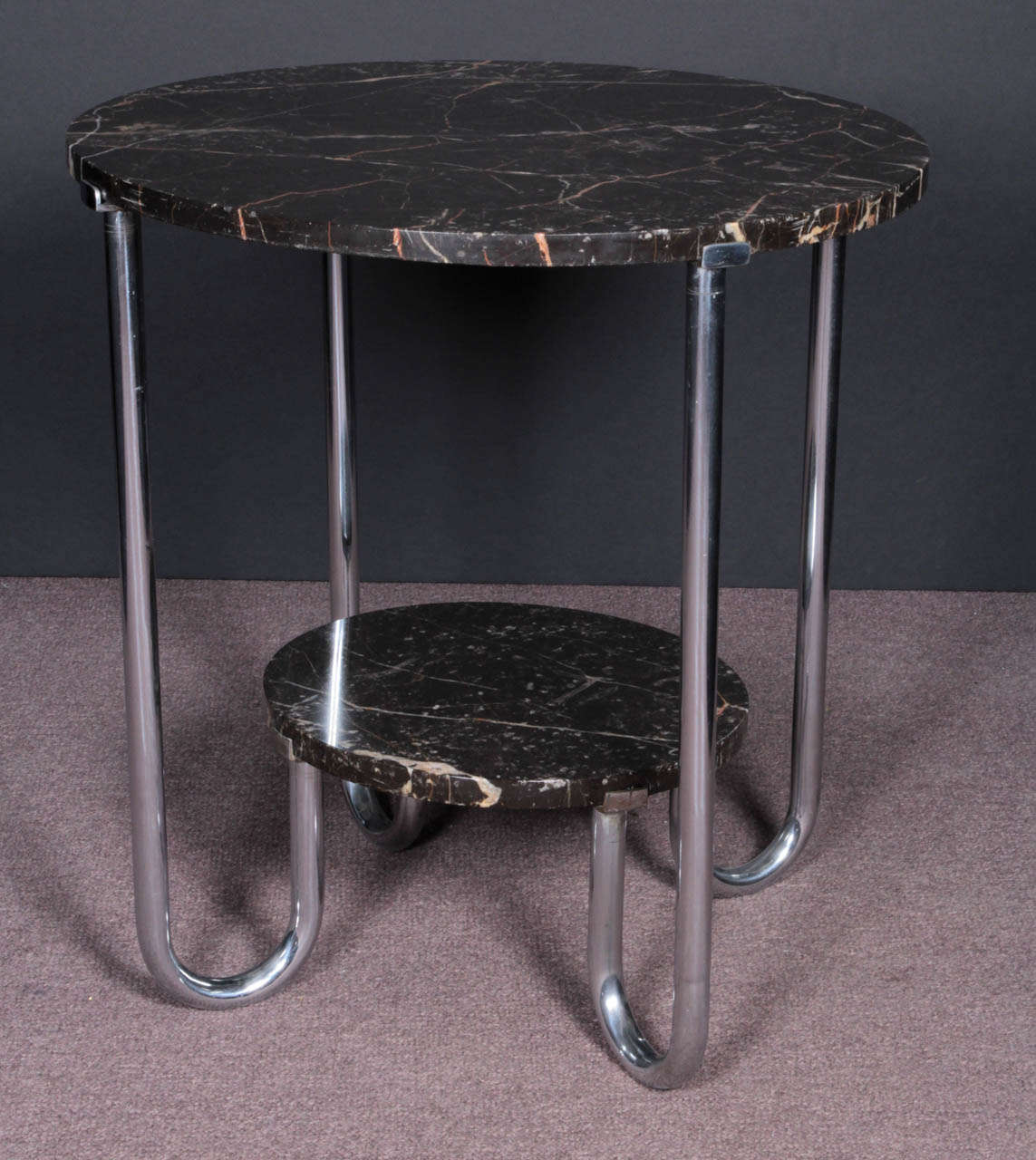 A large circular original marble top supports four tubular chrome legs ending in a curved uplift hairpin turn that hold a smaller second tiered original marble shelf.
Original chrome finish. The marble has a barely discernible hairline fissure along