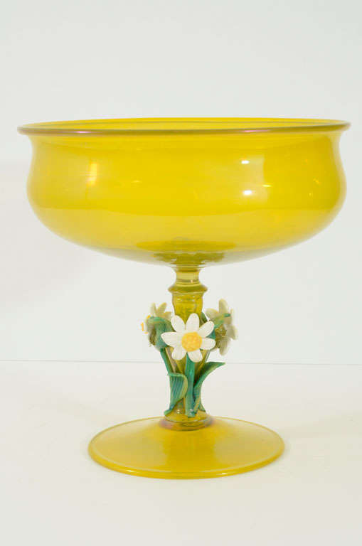 A golden yellow footed glass bowl. The stem ornamented with leaves and white flowers.