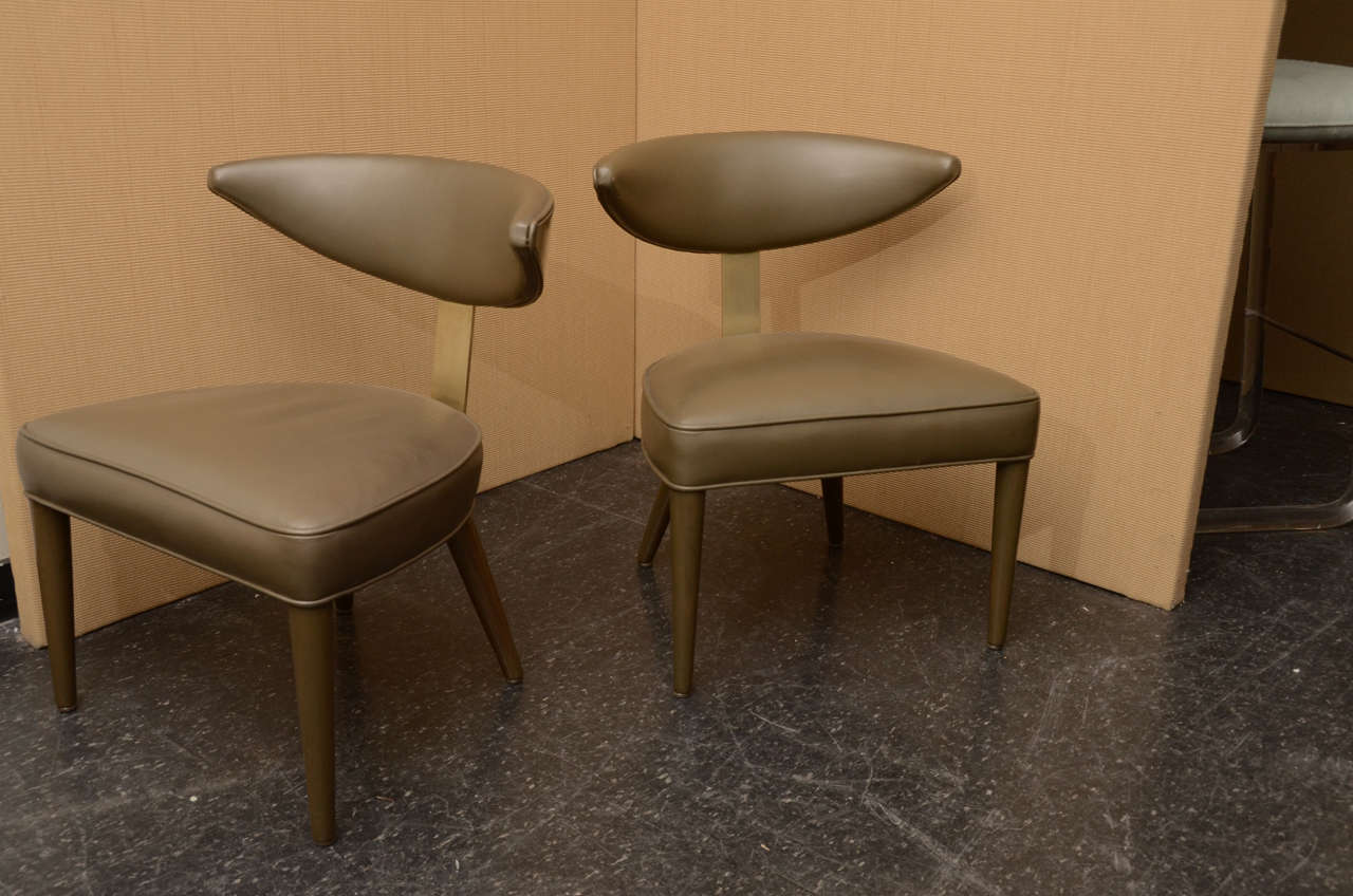 Elegant pair of side chairs my Monteverdi Young. This pair of stylish klismos style back chairs are finished in  an olive stain with brass appointments and green leather upholstery small little hole to one chair seat upholstery