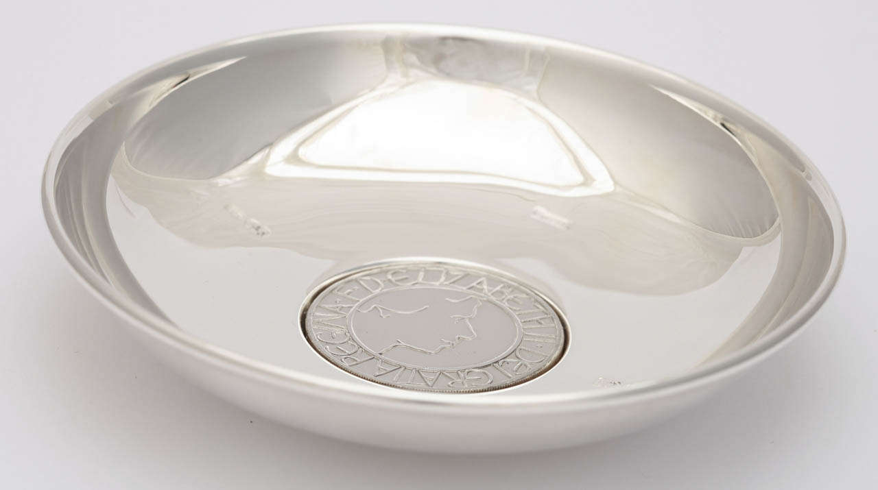 A sterling silver bowl made by Bulgari that features a commemorative coin celebrating the 50th anniversary of Queen Elizabeth II's coronation.  The dish is in the original fitted presentation box . One side of the coin has a Latin inscription which