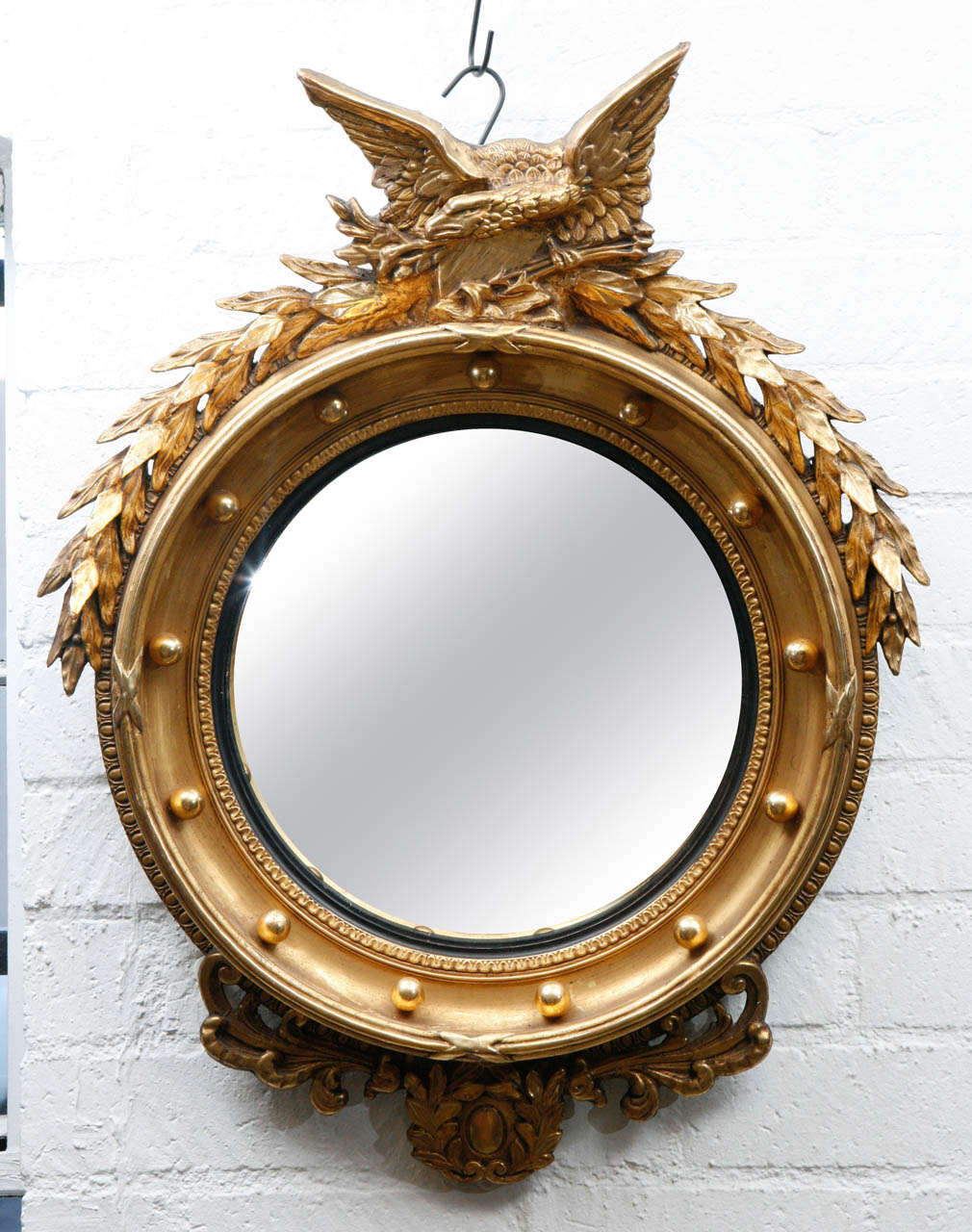 This is a splendidly handsome wall decoration has a large eagle perched on top of a convex mirror swathed in gold decorative elements that are indicative of the federal style of these style of furnishings.  This is an exemplary piece well suited for
