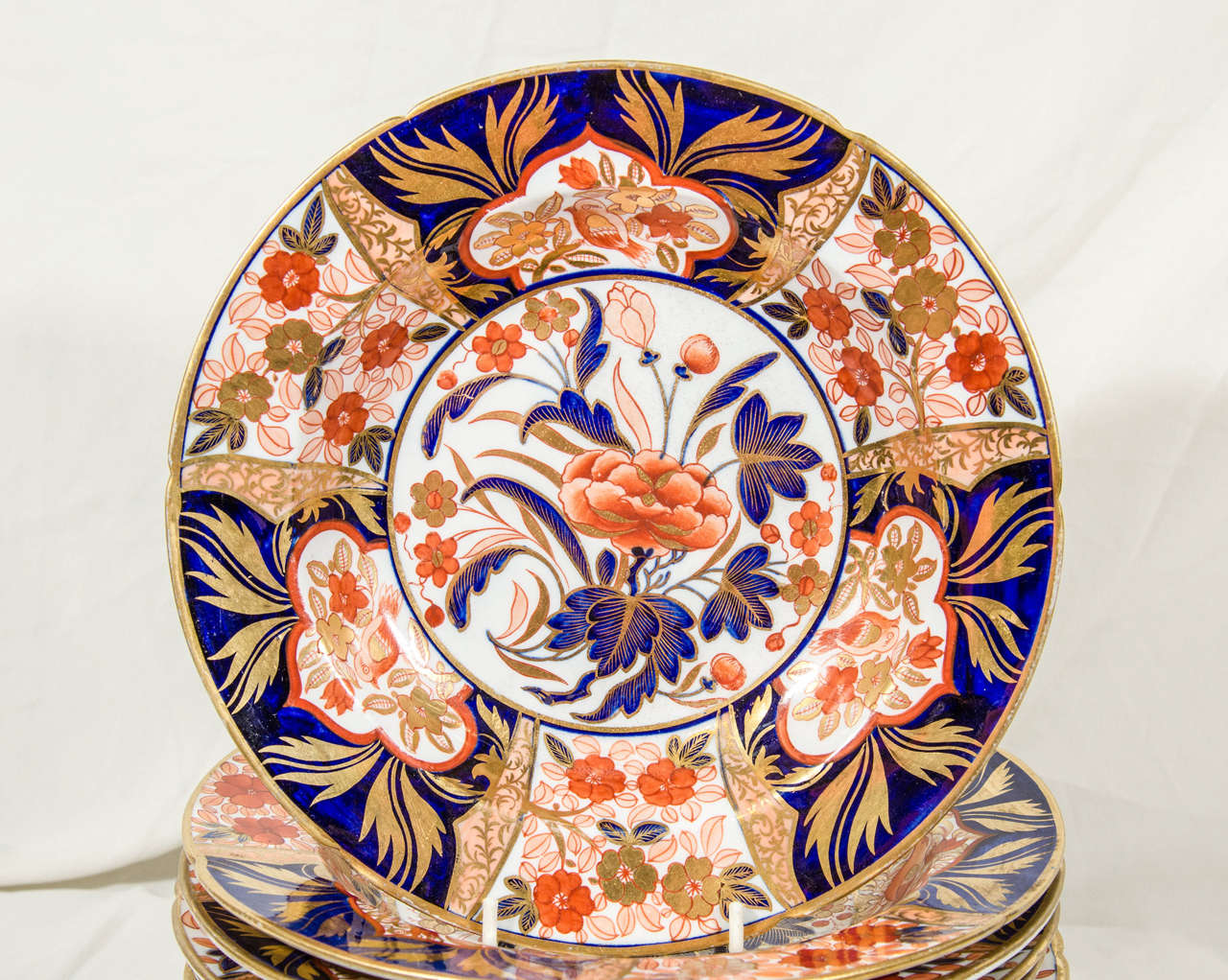 A set of 14 Coalport Imari dinner plates decorated with lavishly gilded cobalt blue and iron red. The pattern features panels and lappets with songbirds centered around a large peony.
Known as the Peony pattern it is a vibrant example of Regency