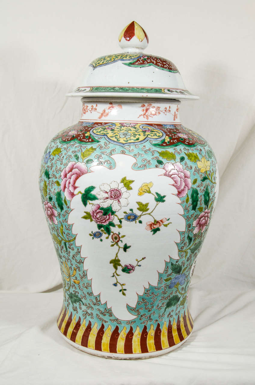 A pair of Chinese Famille Verte covered vases each decorated with green, pink, blue and yellow enamels on a soft green ground. Leaf shaped panels of flowers are reserved on a white ground. The cover, the shoulders, the finial and the base of the