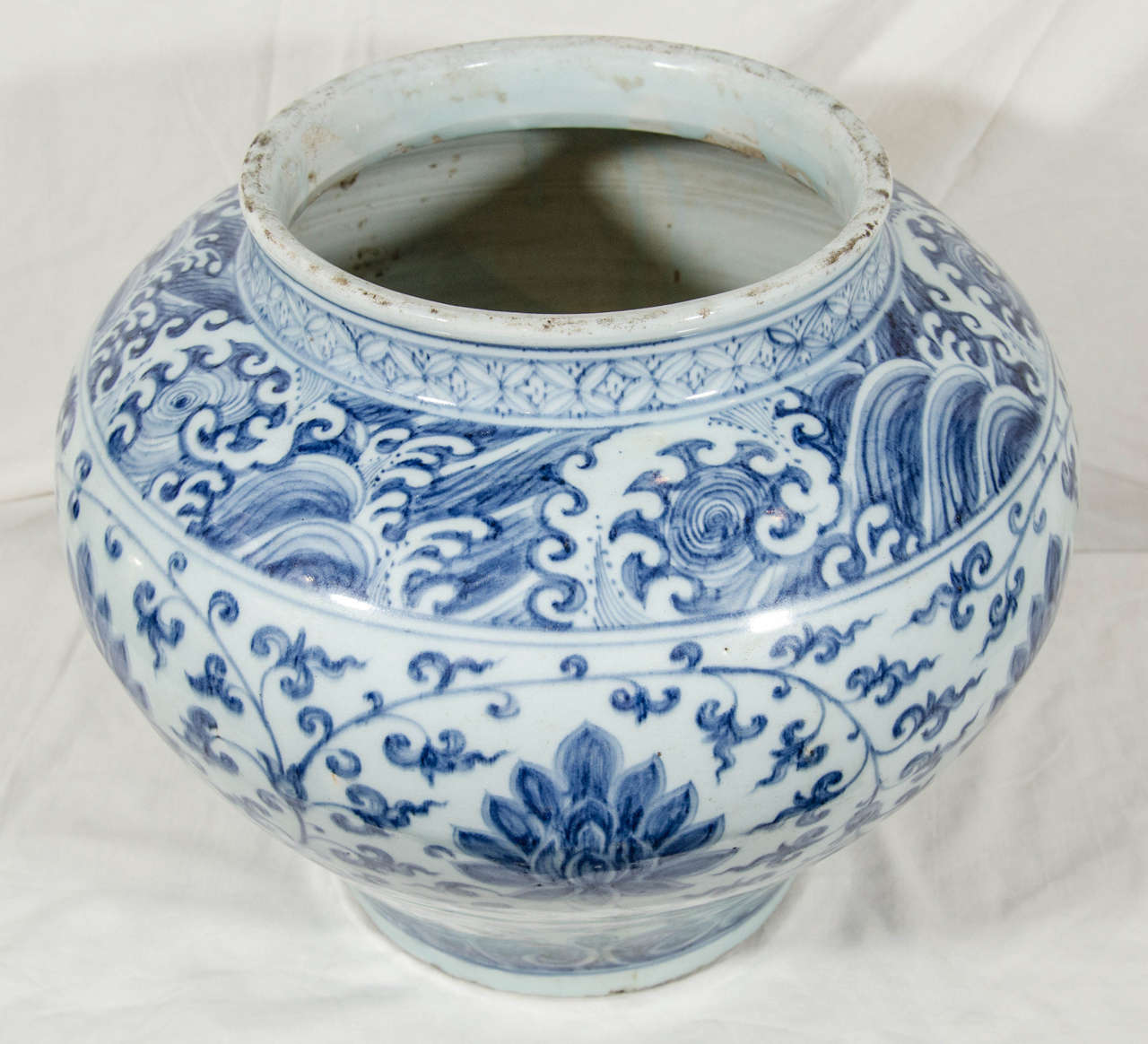 A Chinese Blue and White wine jar decorated in cobalt blue with a band of crashing waves around the neck, lotus flowers in a broad band around the body, and a band of leaves in a border at the base.The cobalt blue was painted onto the white surface