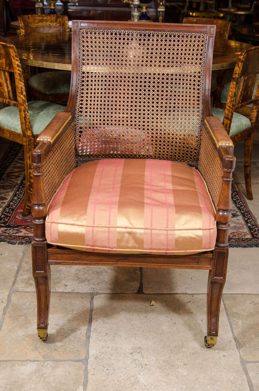 Regency cane-filled library bergère with loose cushion seat, padded arms and sabre legs ending in casters.