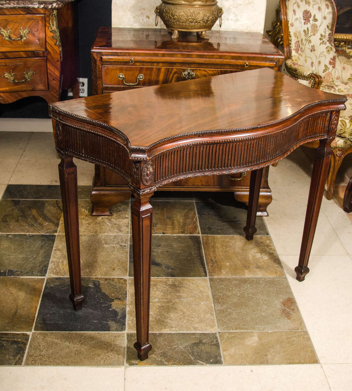 George III mahogany serpentine flip-top card table with fluted frieze and tapering square legs headed by paterae, with a traditional green baize lined interior.