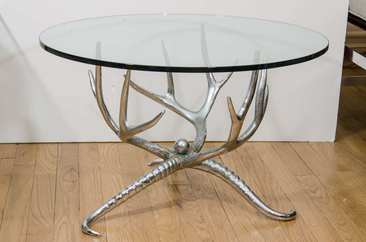 Small circular glass top table with nickel horn form base.