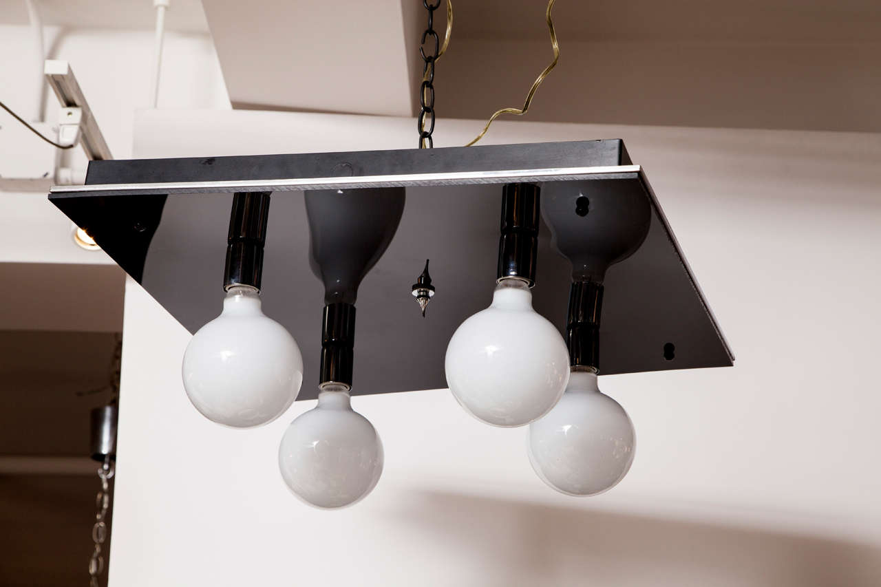 A modernist flush-mount light fixture crafted from black glass and chrome.  USA, circa 1970.  Features a black glass panel accented with chrome; four standard sockets hold oversize globe bulbs; 100 watts each max.