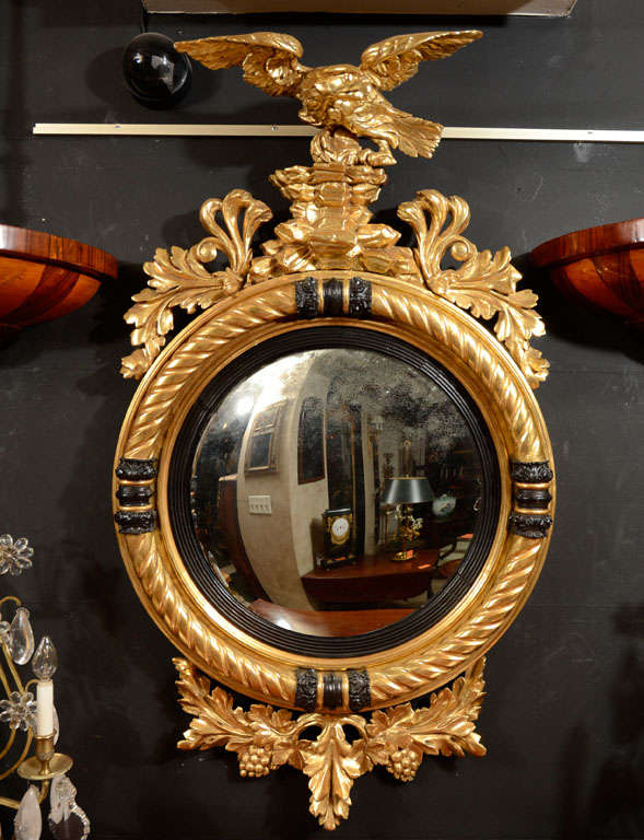 Carved gilt wood convex mirror with eagle mounted on rockery, oak leaves above an ebonized and gilt rope twist framed mirror.