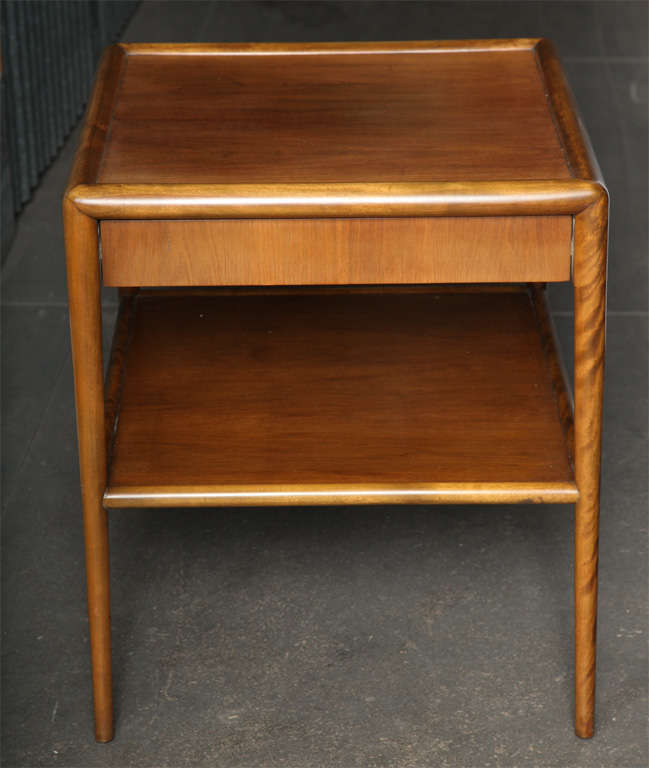 Light walnut and walnut veneer two-tier side tables with a hidden plinth drawer. An unusual and rare execution of an iconic table by Robjohn-Gibbings for Widdicomb, which is more commonly found without drawers. Each has fabric label in drawer.