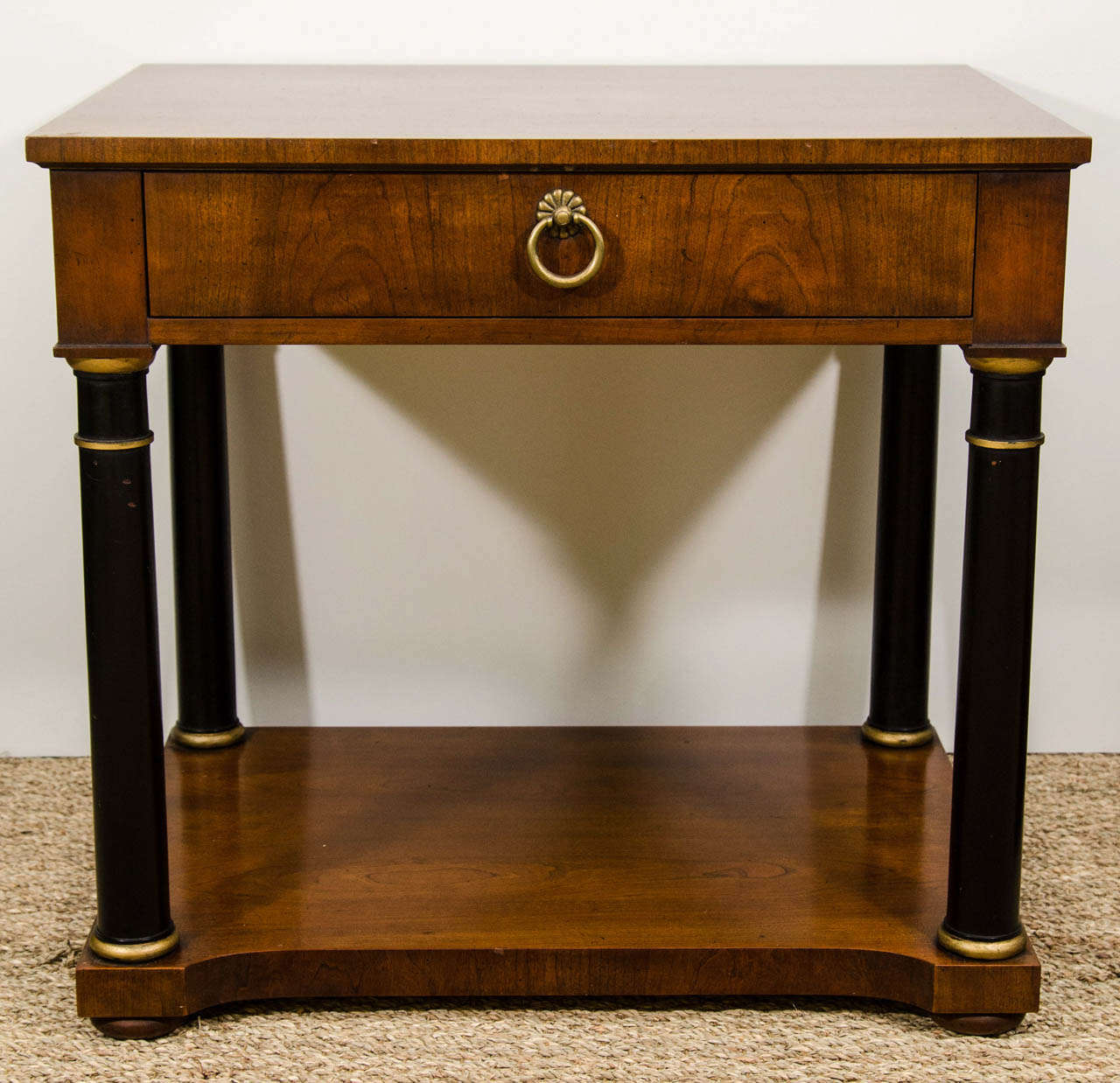 A pair of neoclassical style small side tables in mahogany with ebonized and parcel gilt columns.  Each table has one drawer and a lower shelf.