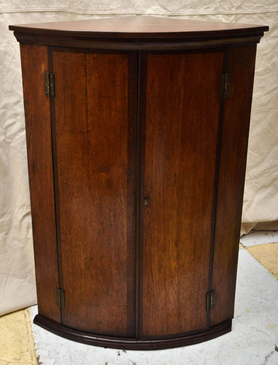 English George III oak mahogany cross banded bow front hanging corner cupboard with later oak top. This type of cupboard would have originally hung from a corner. Now it can be used on the ground or hung in a corner.  Great for storage in a bathroom