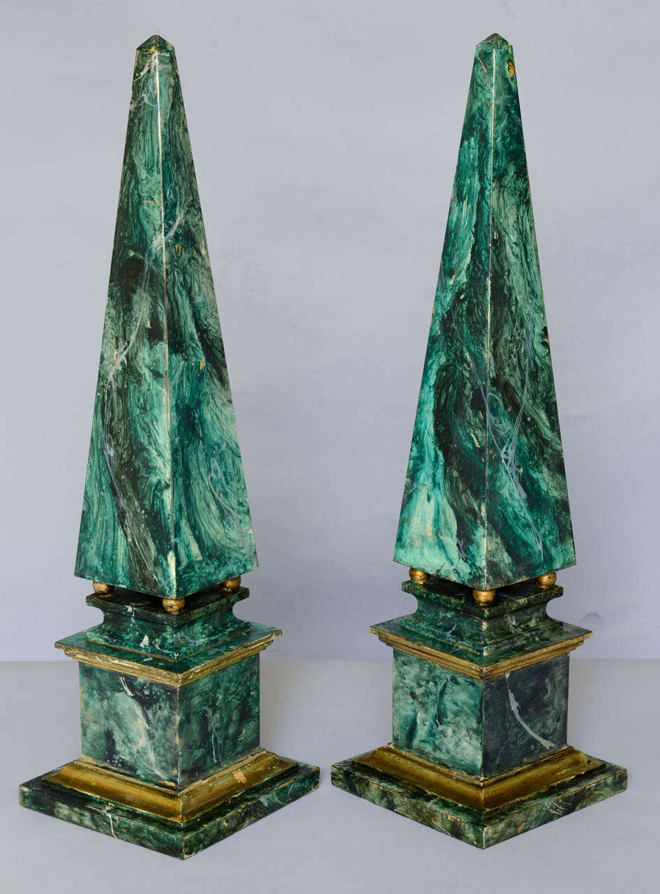 Pair of vintage obelisks, of handpainted wood, on ball feet, raised on graduated square plinths, each faux painted as green marble with parcel gilt accents.

Stock ID: D3013