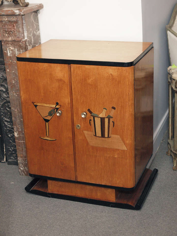 Glamorous maple veneer Art Deco German rectangular bar cabinet.  The cabinet is raised on a rectangular pedestal which is in turn situated on a low black lacquer-accented scrolling base.  The front edges of the cabinet are curved and the top is