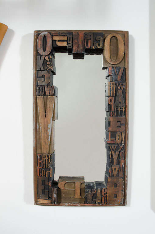 A graphic three-dimensional framed mirror comprising letters in various sized woodcuts on a sturdy wood and cement back. Stamped 'Jo Mead'. U.S.A., circa 1960.
