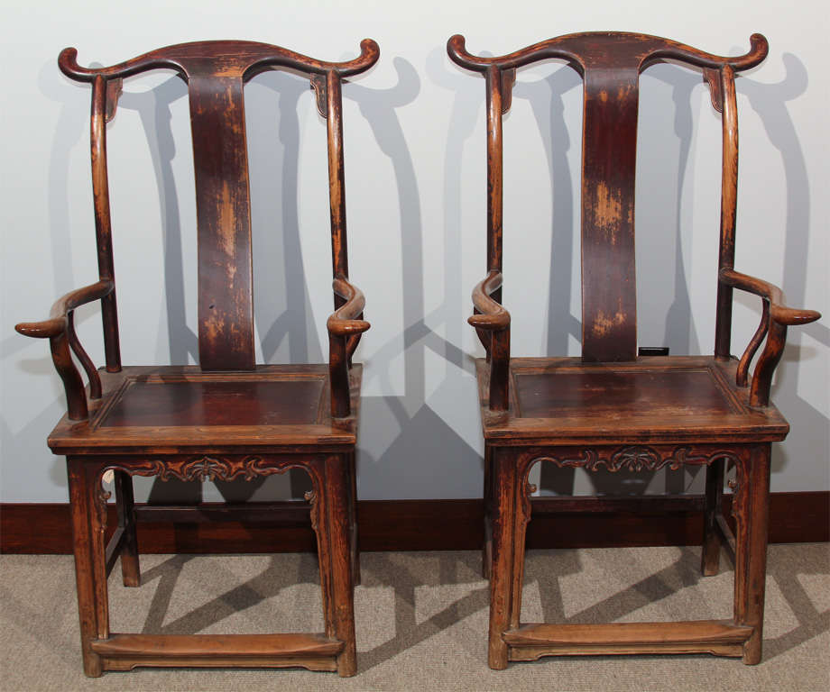 A pair of Chinese yolk-back arm chairs (fushouyi). Constructed of elm wood (jumu), the chairs with curved crestrails and back splats, the square legs with carved aprons, side and back stretchers and foot rails. The chairs with wiped lacquer finish,