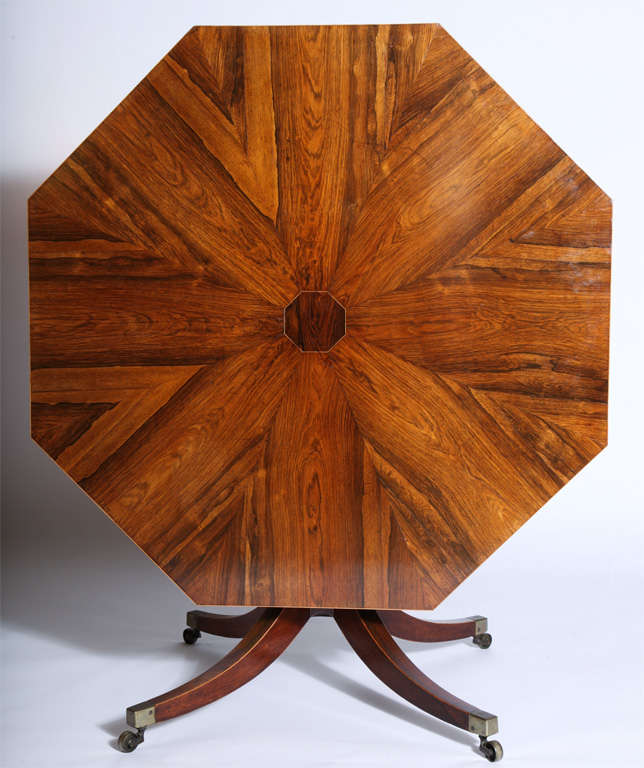 A Regency rosewood octagonal center table, the top with radiating veneers and boxwood strung border, on an octagonal standard continuing to four splayed legs terminating in casters.