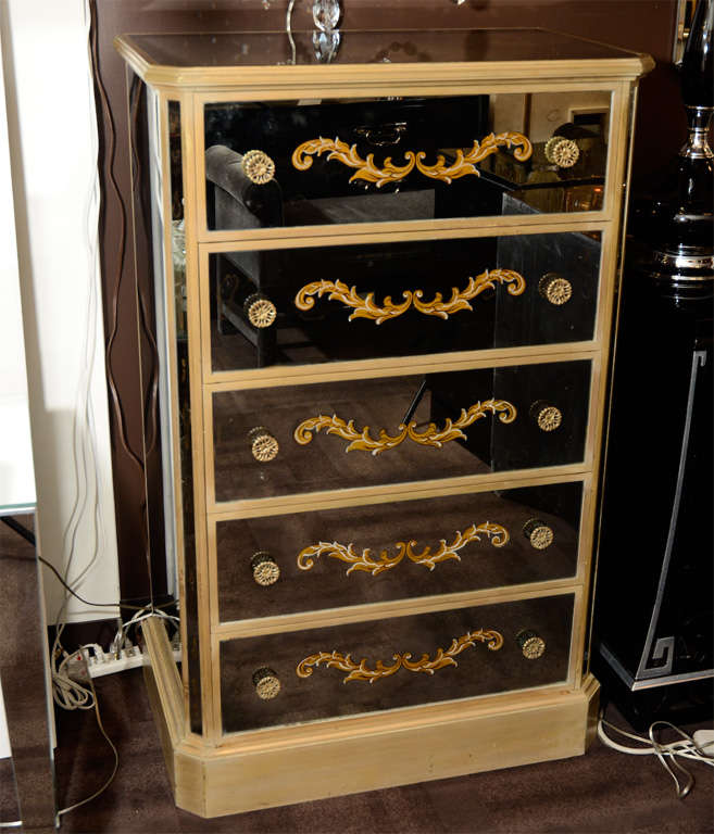 This stunning chest features five drawers with reverse stylized acanthus églomisé detailing on smoked mirrored fronts. The handles are gilt as well as the trim and detailing. The sides and top of the commode are also inset with smoked mirrored