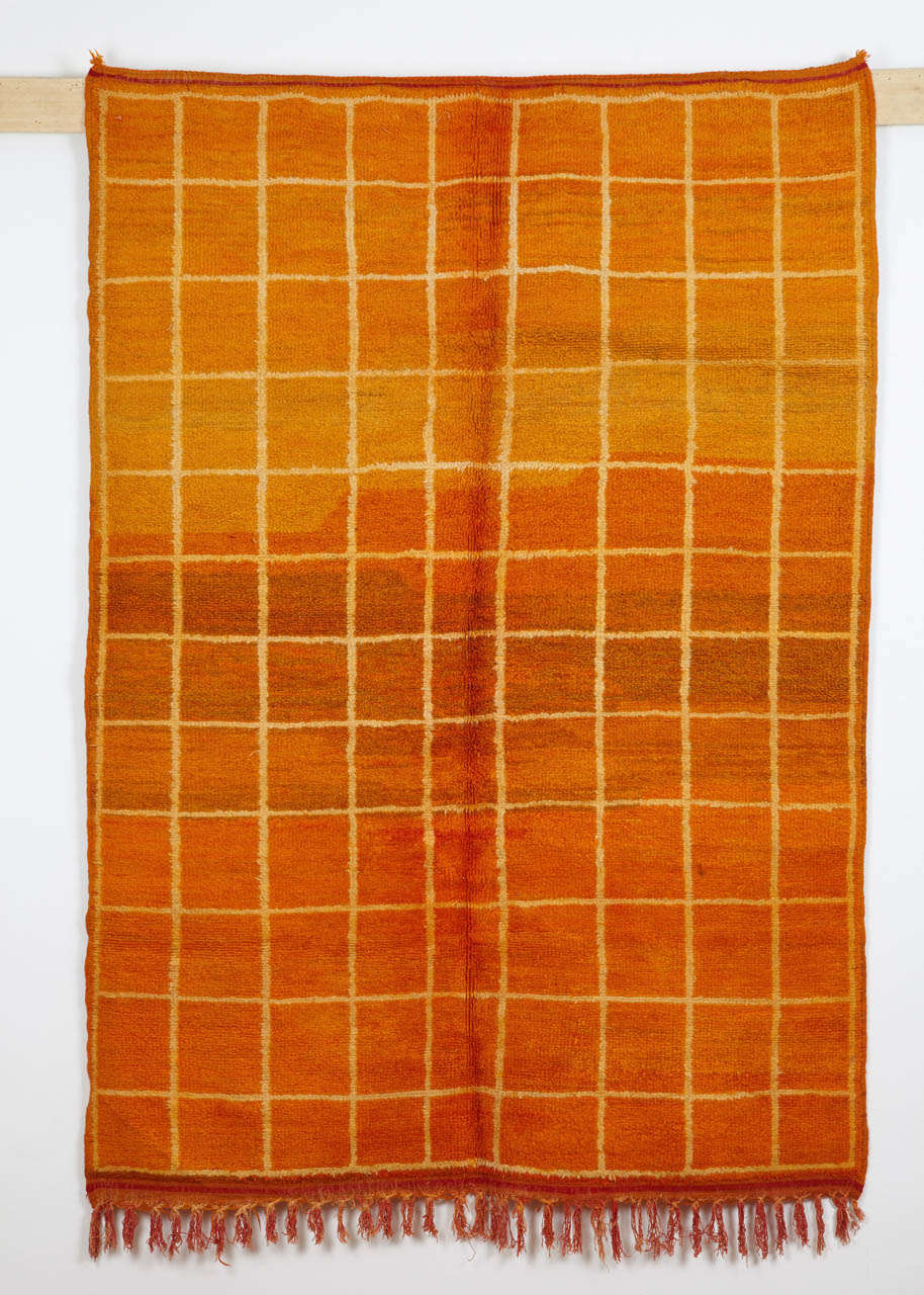 The rugs from the Oulmes region in the Moroccan Middle Atlas are typically on an orange-red background, where this can be in a variety of shades. This example is further embellished by a square grid superimposed in a lighter shade.