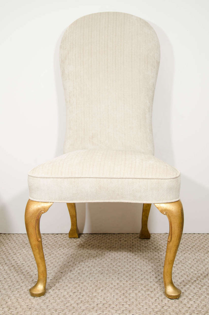 A set of glamorous Queen Anne Style dining chairs with giltwood cabriole legs and a tall, rounded back.  The chairs have been newly re-upholstered in a light beige velvet.  Although these chairs are traditional, they feel fresh and modern and would