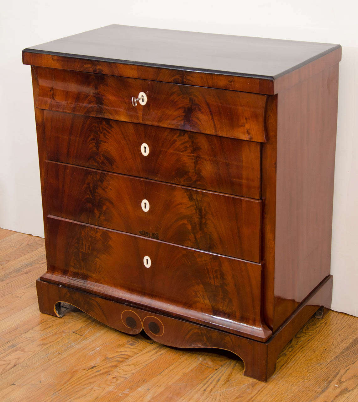 Elegant and restrained with four drawers, the upper and lower of which splay outwardly at the base, the chest is adorned with flame mahogany veneers which carry from the ebonized bevelled upper edge to the whimsical ebony and birch inlay of the base.