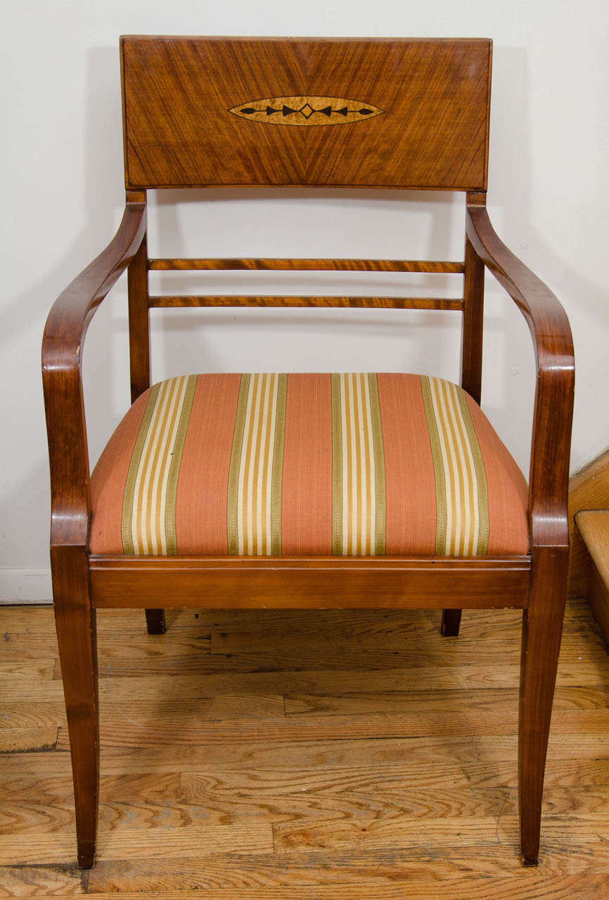 A sleek pair of solid birch and palisander chairs with a stylized inlaid crest of burled birch and mahogany, which adorns the backrest. Gracefully sweeping arms transform into slim sabre legs. The period appropriate upholstery is immanently usable