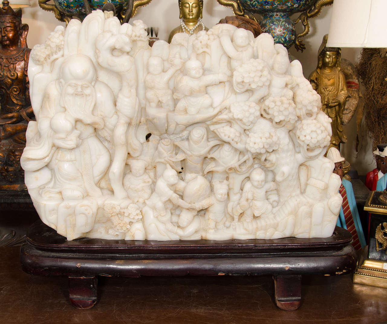 A Chinese white jade sculpture with intricate carving of Shou surrounded by children. Shou is holding a cane and peach. He is the God of longevity.

Good condition with age appropriate wear. Some staining to the jade and one area is unpolished.