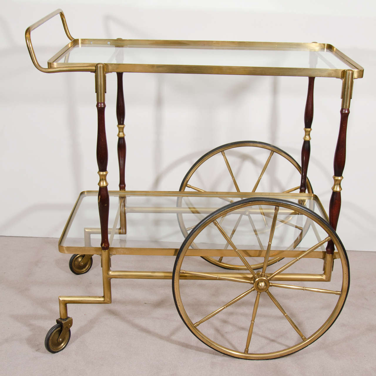 A vintage 1950s brass and wood bar cart with two glass shelves, and rubberized wheels. Made in Italy.

Good vintage condition with age appropriate wear and patina. The rubber on the wheels is dried and cracked. A couple of scuffs to wood on one of