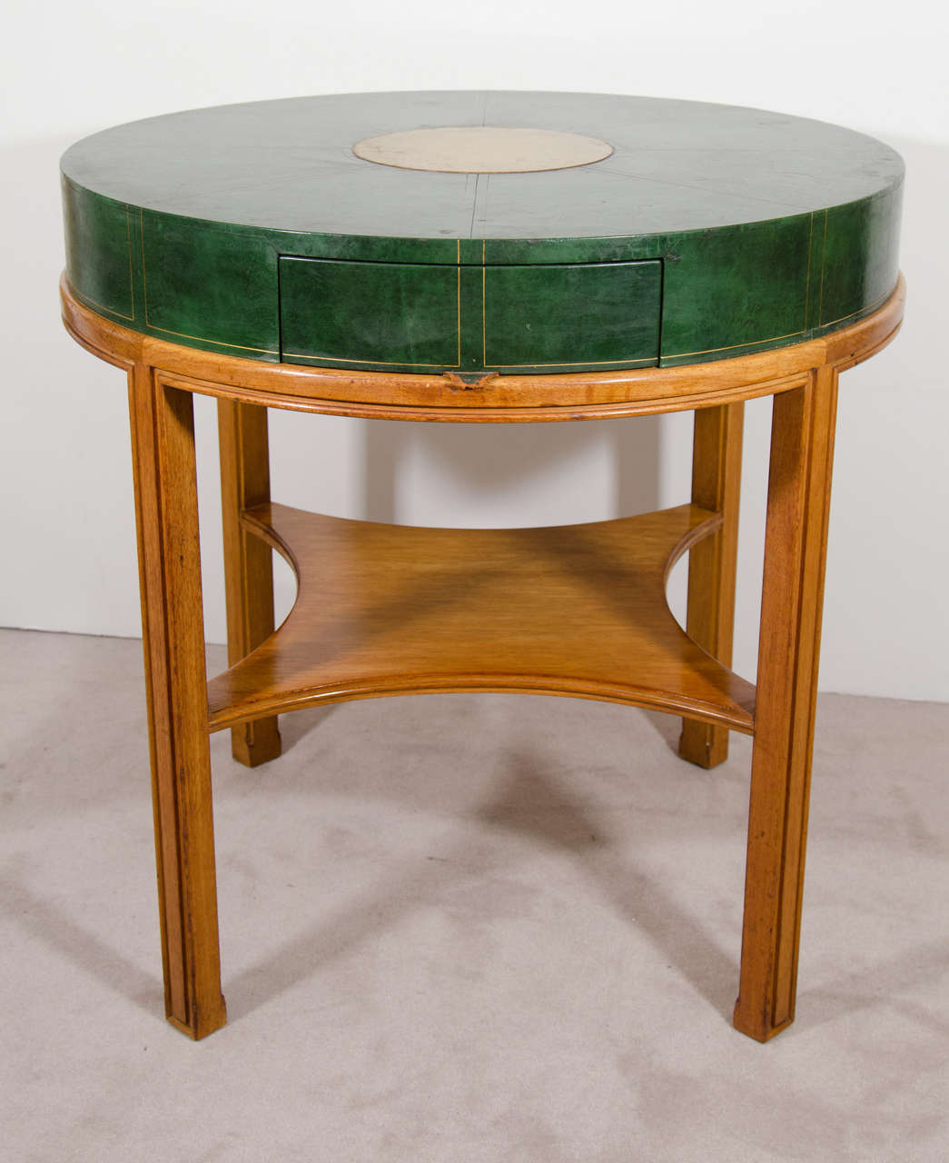 A vintage round leather clad game table by Tommi Parzinger for Charak Modern. Embossed design and gold painted disk in center of the tabletop. There is one drawer with dove tail detailing and a single shelf. The table retains a partial Charak Modern