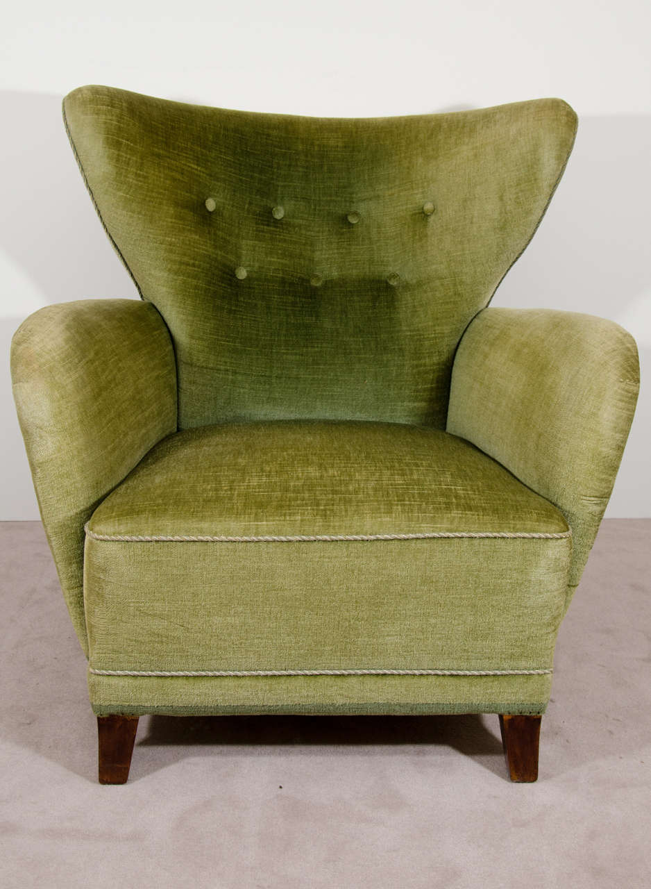 A Scandinavian Modern wingback easy chair with button tufted green plush upholstery and tapering legs.