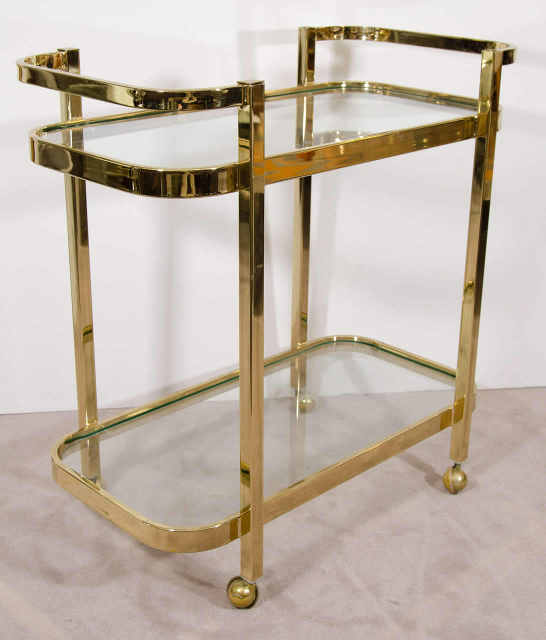 A vintage bar cart in brass plate by Milo Baughman with two glass shelves, and on casters.