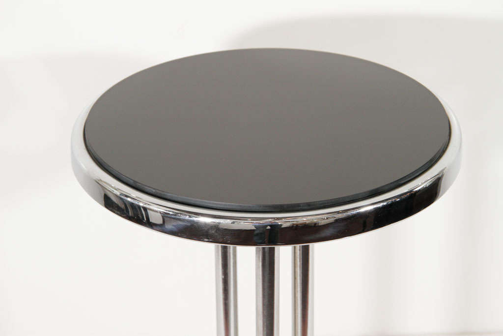 Art Deco side table with Machine<br />
Age design in chrome and<br />
with a vitrolite (black glass) top.<br />
Table has stylized stepped base<br />
with triple cylinder stems and<br />
round top. Perfect side table<br />
between club or