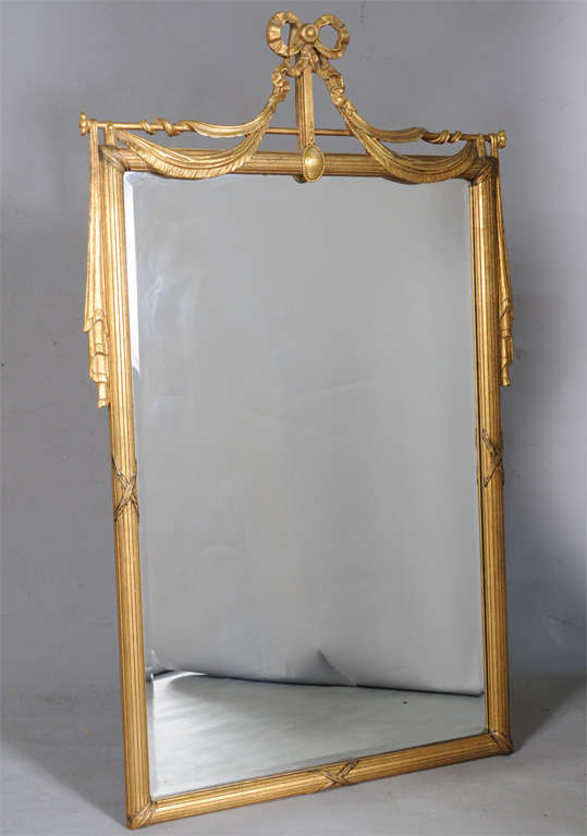 Fine mirror, of carved giltwood, reeded rectagular frame surmounted by a pierced pediment of a bow over swag draped rod.