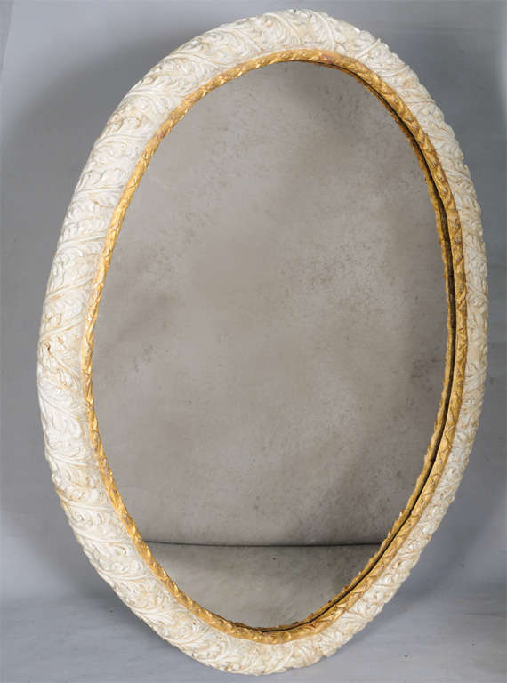 Mirror, of grand scale, painted and parcel gilt, its imperfect oval-form frame hand carved with acanthus and gadrooned border, holding later distressed mirror.