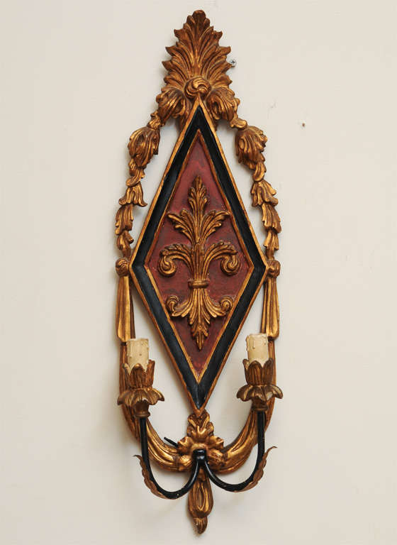 Pair of sconces, of painted and parcel giltwood, each diamond-shaped backplate outcarved with stylized fleur-de-lis, surmounted by palmette flanked by festooning, two iron C-scroll candlearms terminating in foliate bobeches and candlepots holding