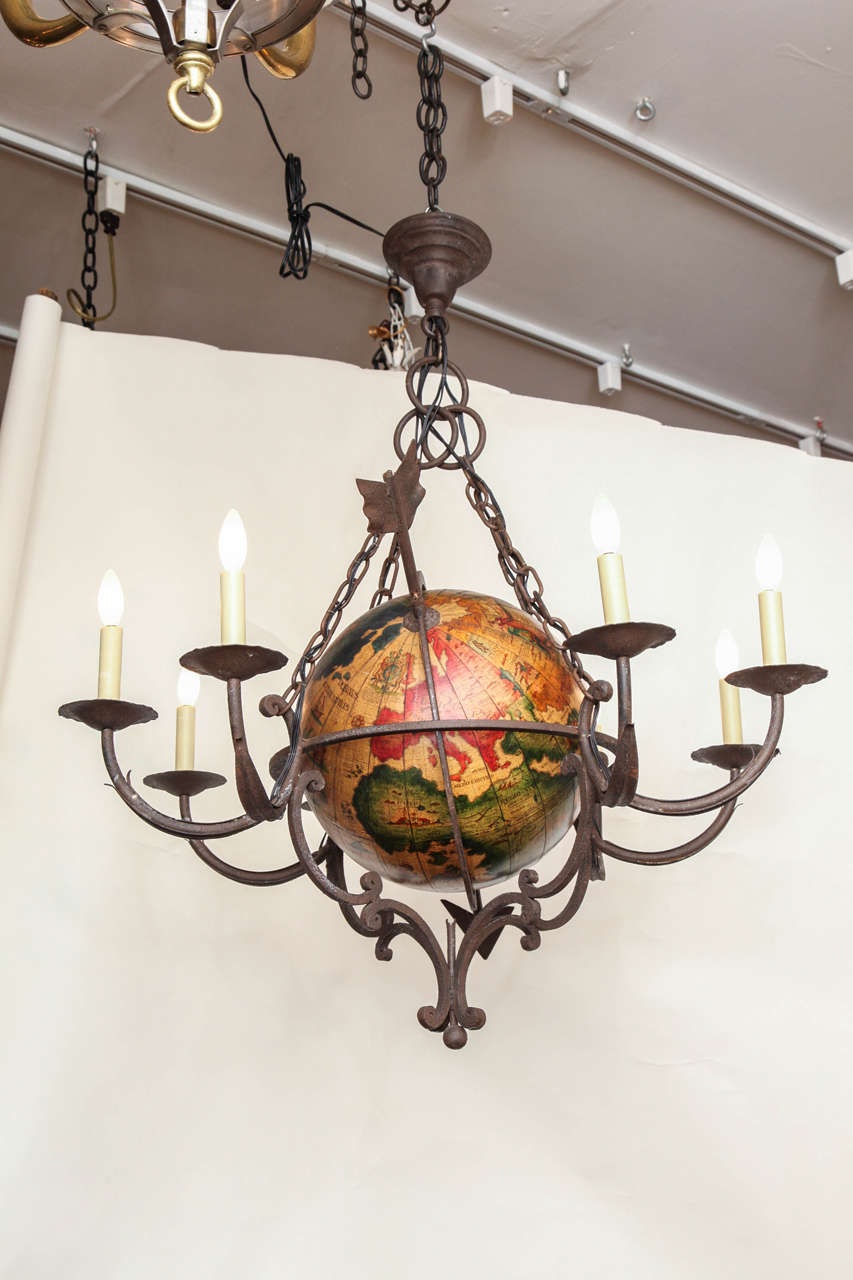 An English 8 light forged Iron Chandelier with ring form center frame holding globe in the style of a 17th century terrestrial globe with hand painted continents and iconography suspended from four lengths of chain and canopy.
