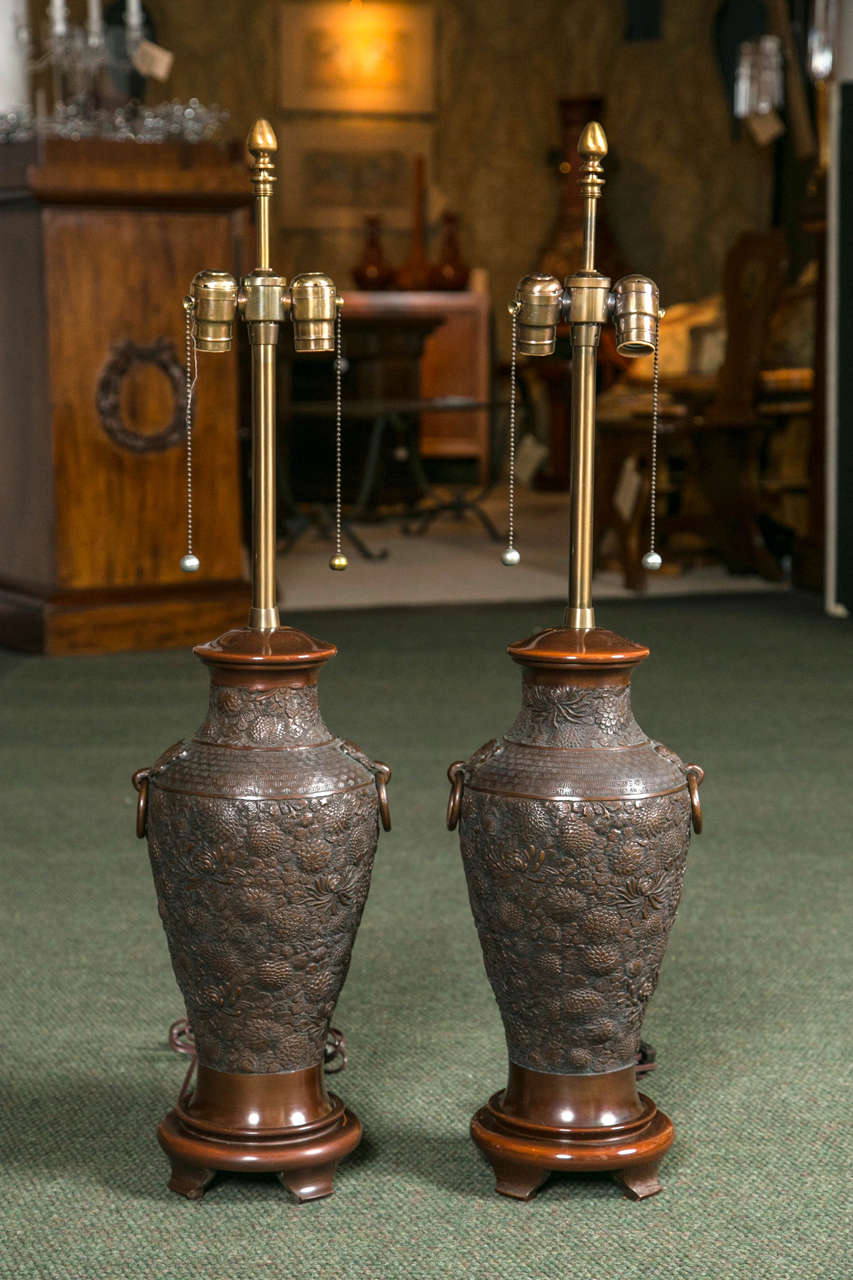 A pair of early 20th century Japanese bronze table lamps heavily and thickly decorated with Chrysanthemums.