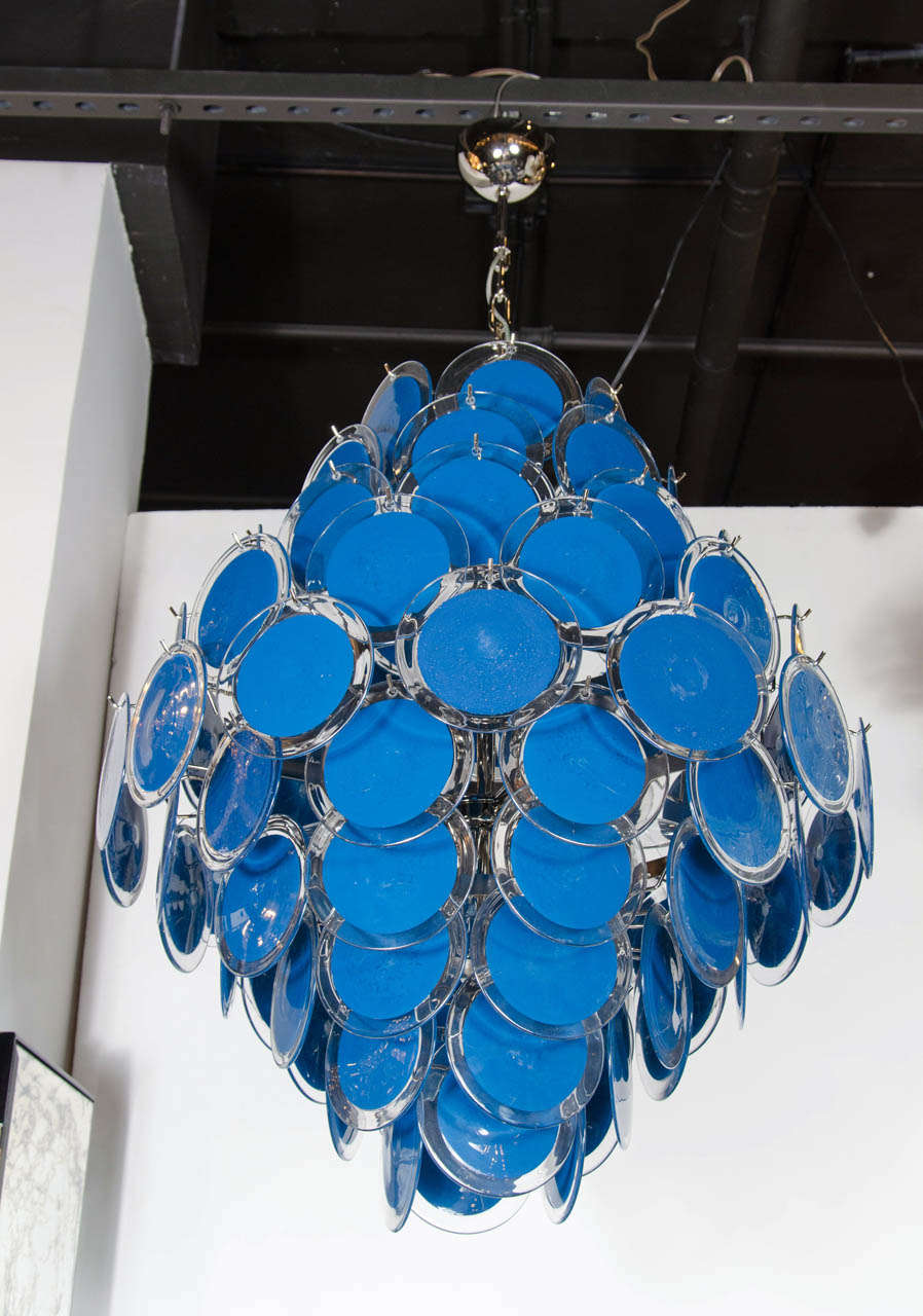 This monumental and striking chandelier realized in the manner of Vistosi, boasts 84 Murano glass discs in a rich sapphire blue- reminiscent of the eponymous shade created by Yves Klein- circumscribed by a clear perimeter. The shades suspended in a