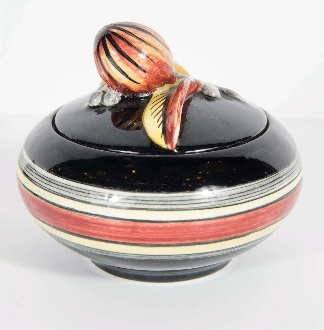 This special round form box features a stylized Art deco foliage design with hand painted accents in pale orange, blue, rust and black. It also features linear concentric detailing.Signed on the bottom with Ilse Claussens initials as well as as the
