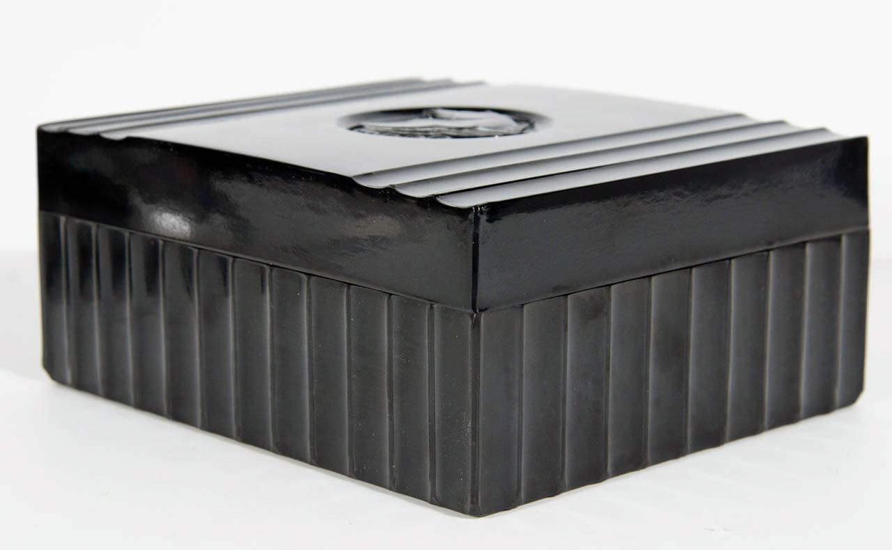Art Deco black bakelite box. This box is made of bakelite and has a ribbed design that is carried on all four sides of the box. The lid has a round inset Pegasus detail in the center and has three ribbed detailing on the outermost sides.