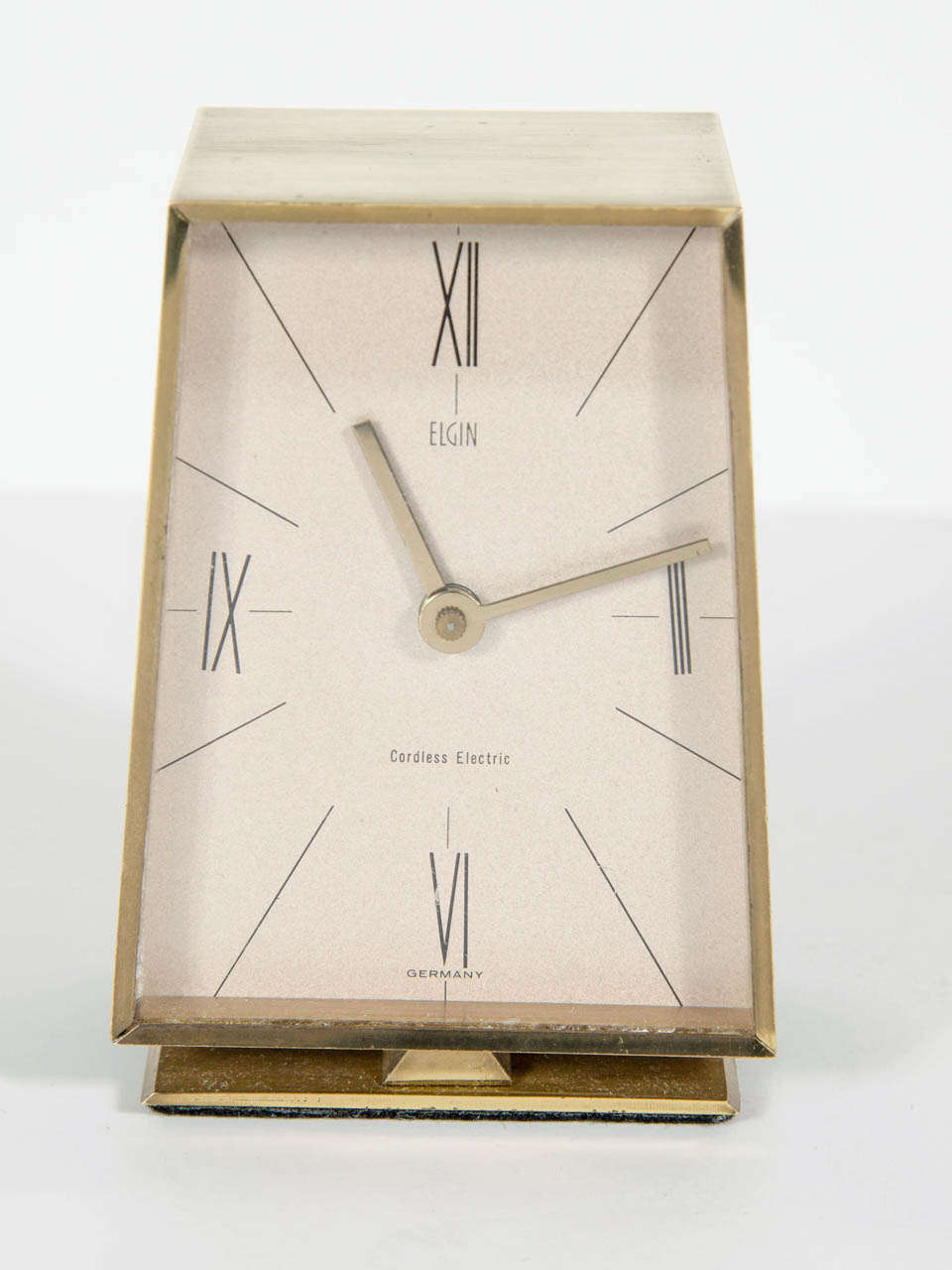 This trapezoidal shape brass clock features a unique mid-century design with black numerals.