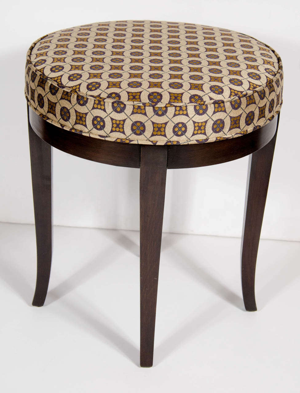This Art Deco stool features a round upholstered seat in a Klimt inspired fabric with geometric design in amber, charcoal and bisque tones. It has out-turned saber legs made of ebonized walnut. This stool has been newly reupholstered and mint