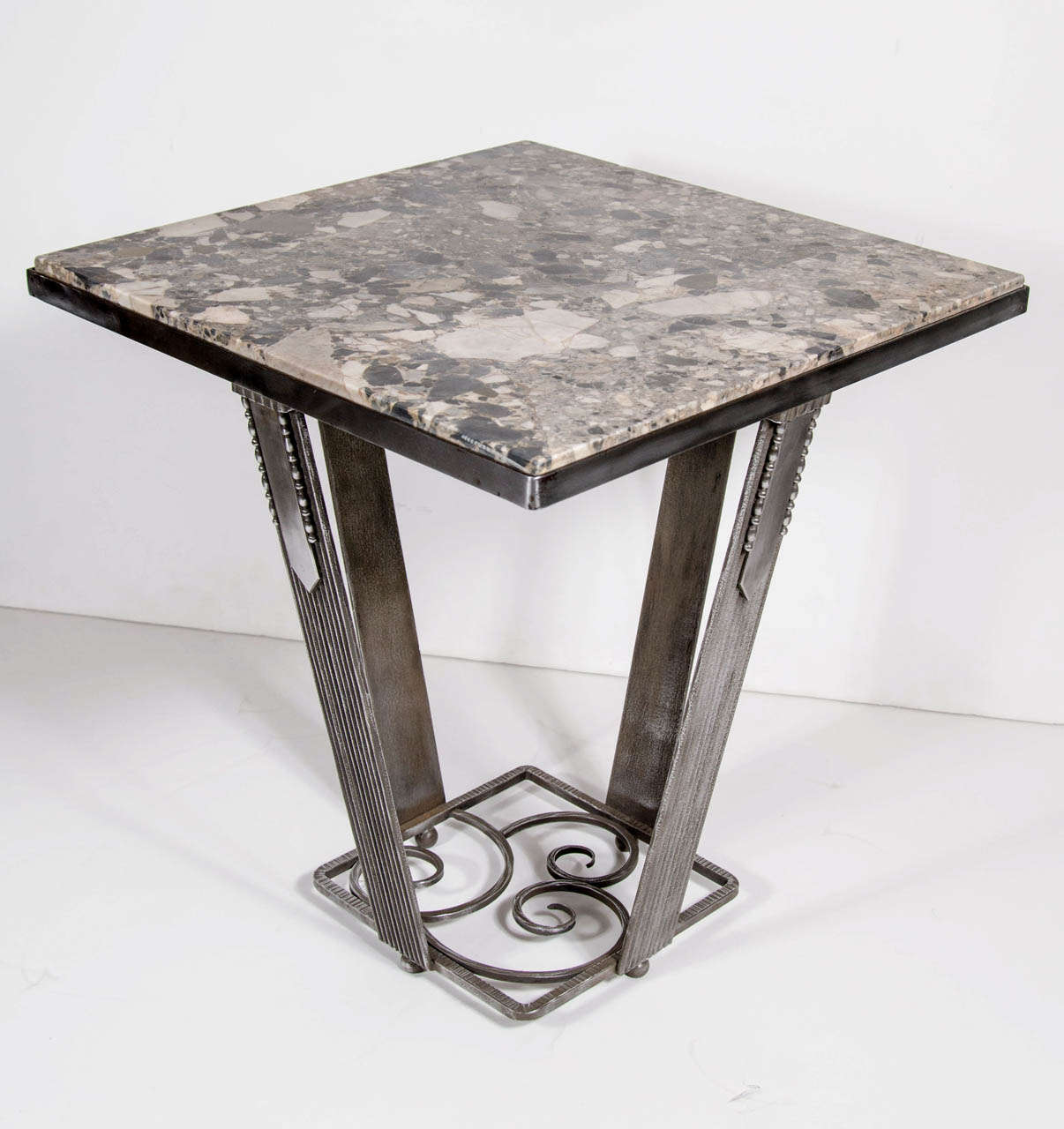 This exquisite table features a exotic marble top in shades of grey and creme resting on a hand wrought iron base . The base features fluted ribbed Art deco detailing with stylized circular accents.The tones of this stunning marble with the tones of