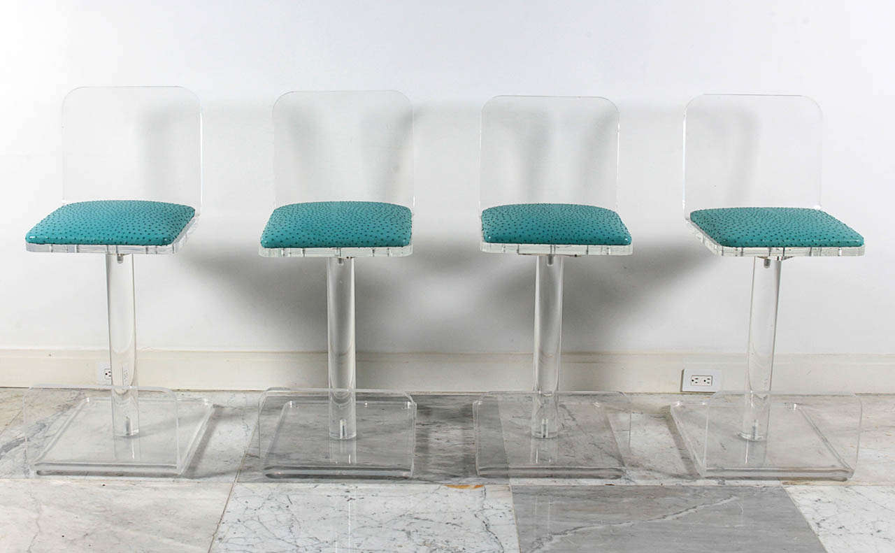 Set of four Karl Springer lucite bar stools with genuine turquoise ostrich leather seats. Stable and substantial. Swiveling seats, non-adjustable bar-height, integral foot rest.