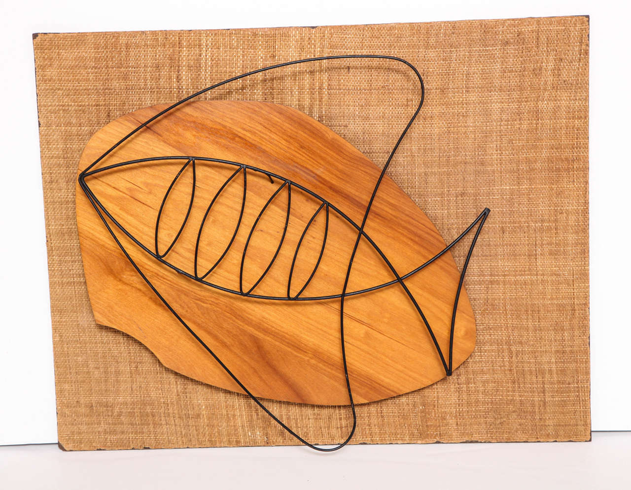 Decorative wall sculpture from circa 1950.
Jute fabric backing with a wood and metal sculpture of a fish.
The jute fabric has some worn off edges all around.