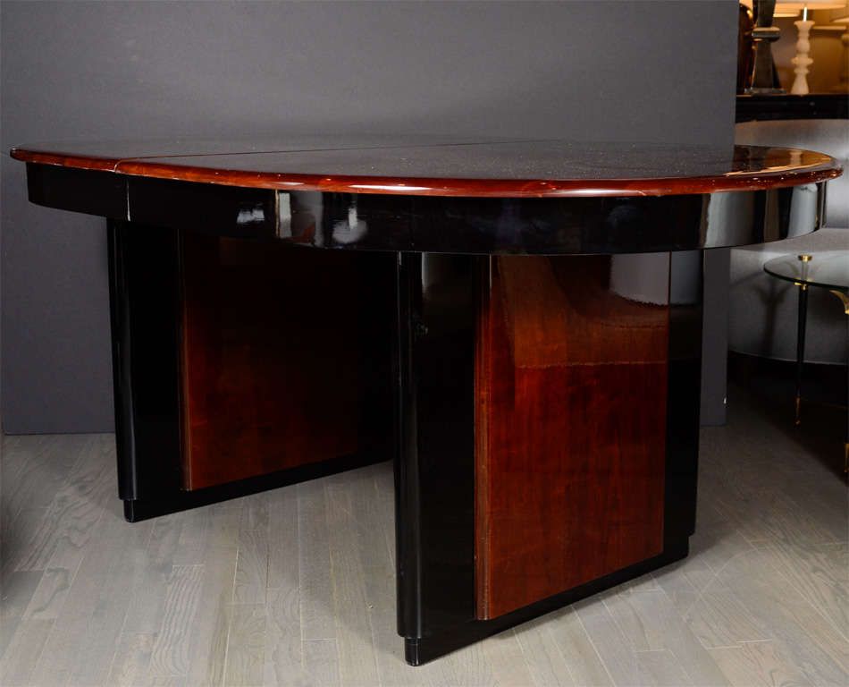 This stunning Art Deco Machine Age table was realized in the United States circa 1935. It features an oval streamlined top in mahogany wrapped in black lacquer. This banding detail recurs on the skyscraper style supports, which feature mahogany