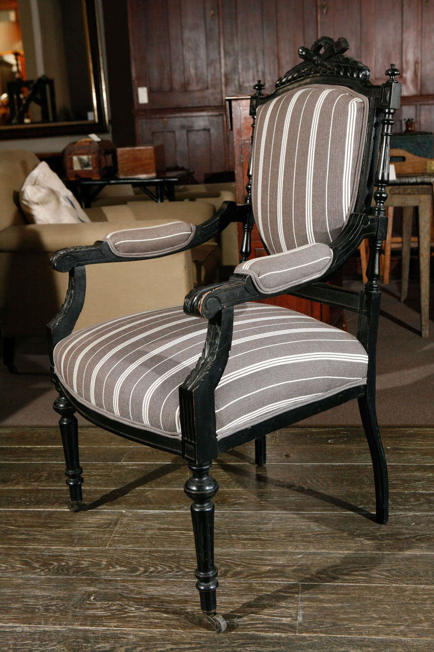 1870s Louis XVI style ebonized fauteuil. Ebonized and carved open armchair with striped upholstered linen and front castors.