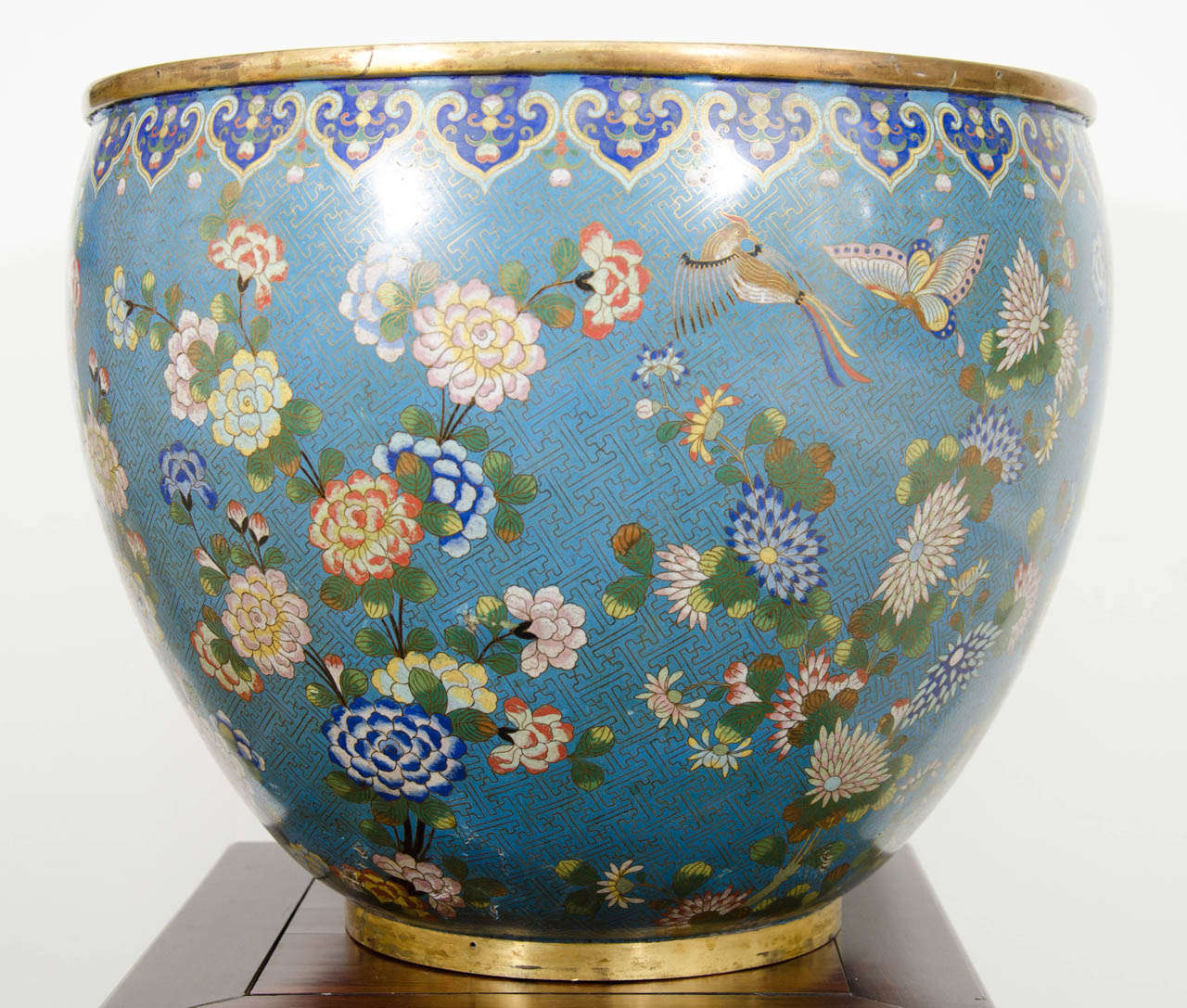 A large Chinese 19th Century Daoguang Period cloisonne fish bowl or planter decorated with multi-colored, flowers, birds and butterflies on a turquoise ground of gilt bronze fretwork and beneath a top border of cobalt blue and yellow ruyi shapes